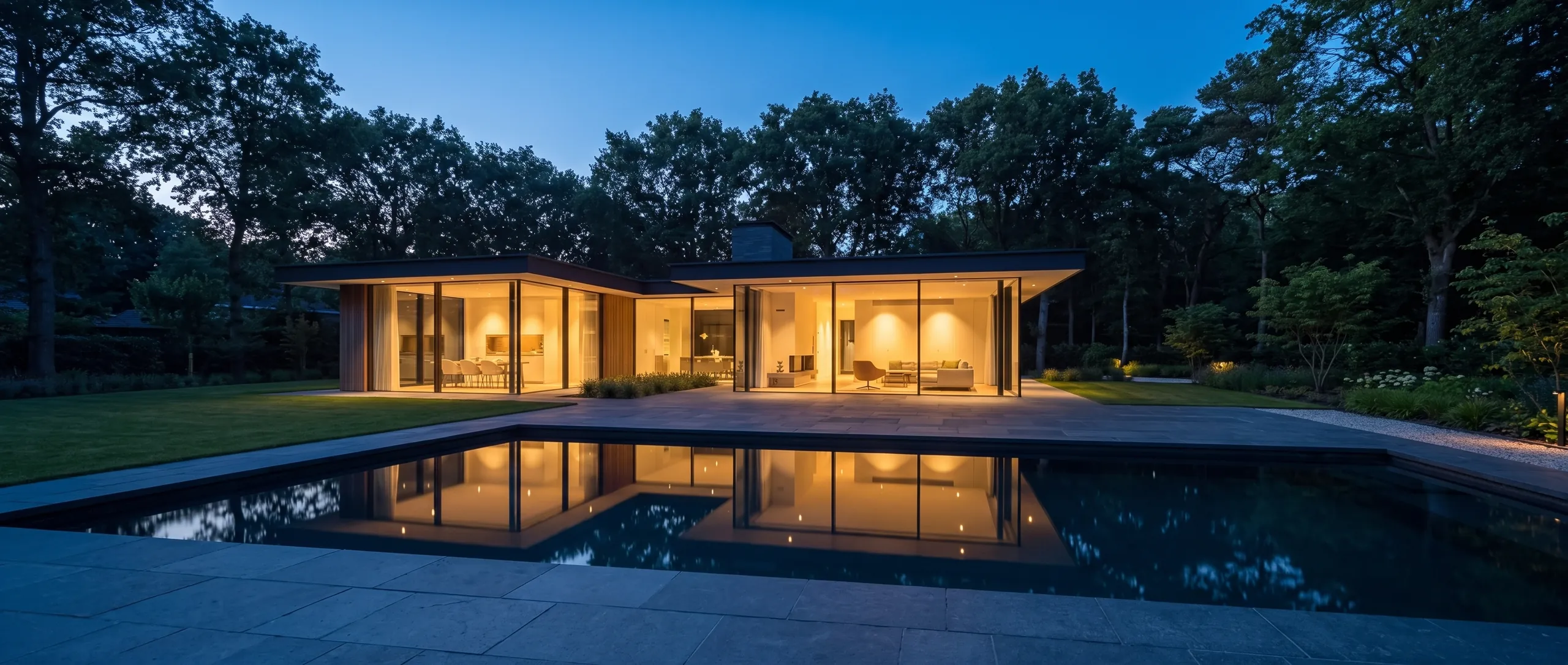 Maison contemporaine au crépuscule, baies éclairées, bassin miroir.